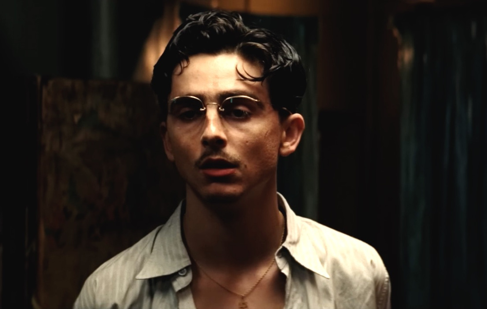 Timothée Chalamet with parted dark hair and a thin mustache in Marty Supreme